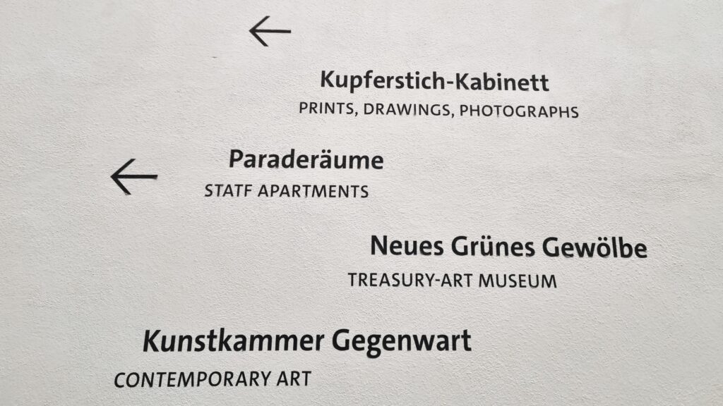 Das Bild zeigt einen Wegweiser aus dem Innenhof des Dresdner Schlosses. Kupferstichkabinett, Paraderäume, Neues Grünes Gewölbe, Kunstkammer Gegenwart sind ausgeschildert. Es soll verdeutlichen, dass Werke von Käthe Kollwitz im Kupferstichkabinett besichtigt werden können.